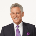 Bill Ritter with short, curly gray hair wearing a purple patterned tie, matching pocket square, and a dark suit against a plain background. The 2023 Manhattan Jewish Hall of Fame Inductee exudes confidence and elegance in his formal attire.